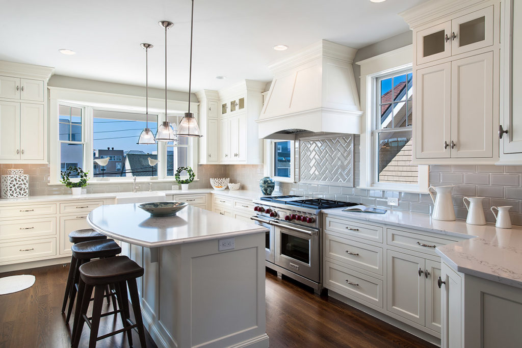 Beautiful white kitchen with commercial stone and ovens and island with wood stools. 